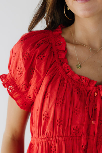 Close view of a young woman wearing a red eyelet blouse with short puff sleeves and a scoop