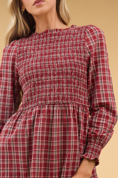 Close view of a woman wearing a red plaid dress with a smocked bodice and long sleeves.