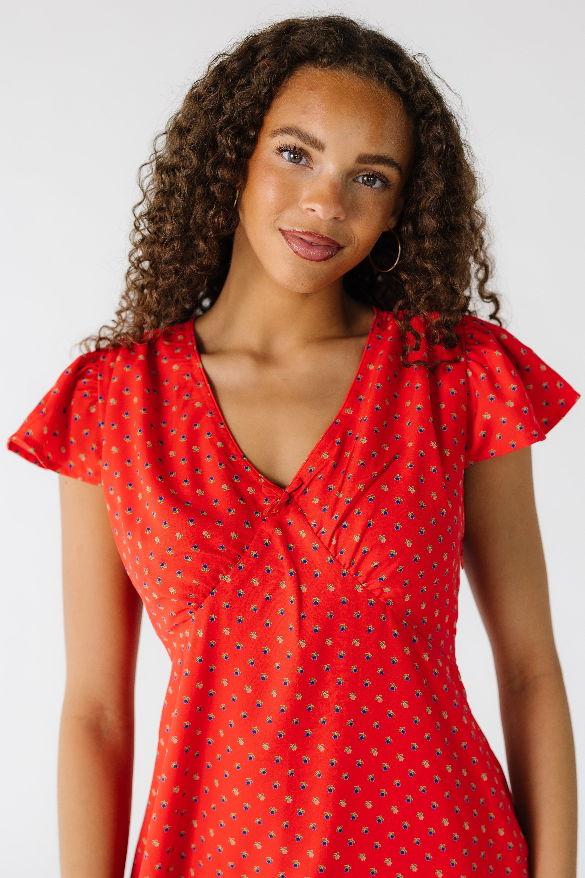 Close view of a teen girl wearing a red print dress with a pointed empire waist, V-neckline and short flutter sleeves.