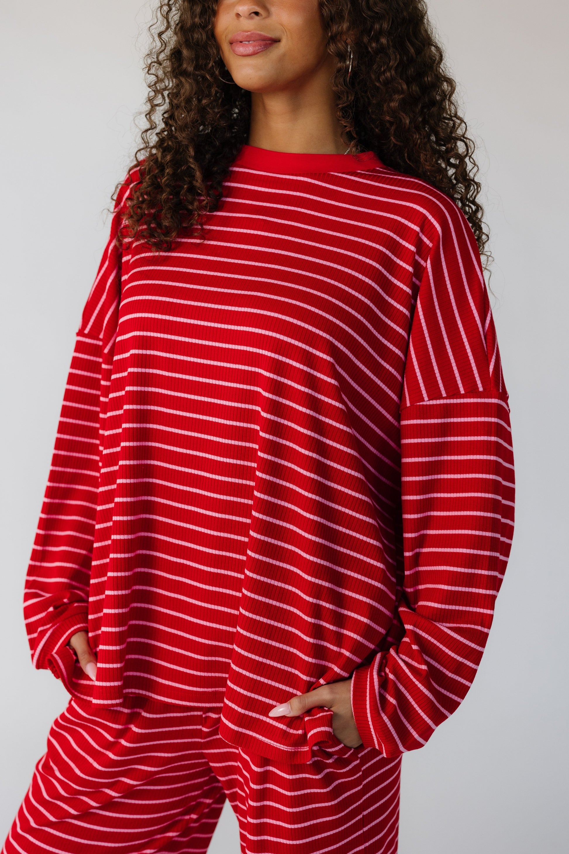Close view of a teen wearing a red ribbed lounge set with pink stripes and side pant pockets.