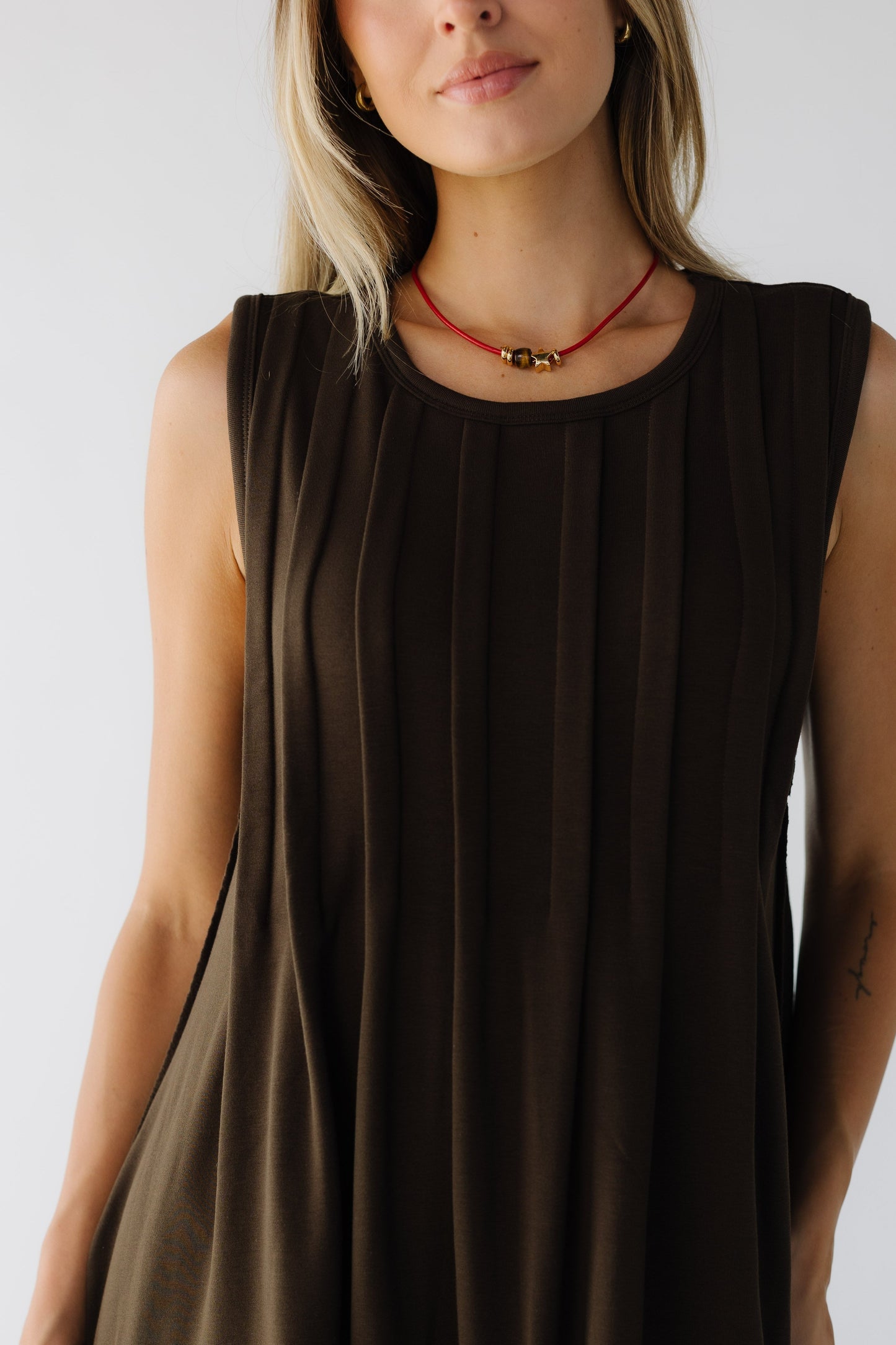 Close view of a woman wearing a brown sleeveless pleated dress with a round neckline.