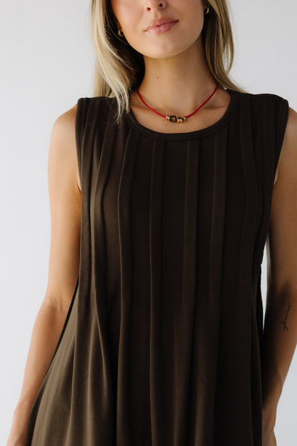 Close view of a woman wearing a brown sleeveless pleated dress with a round neckline.
