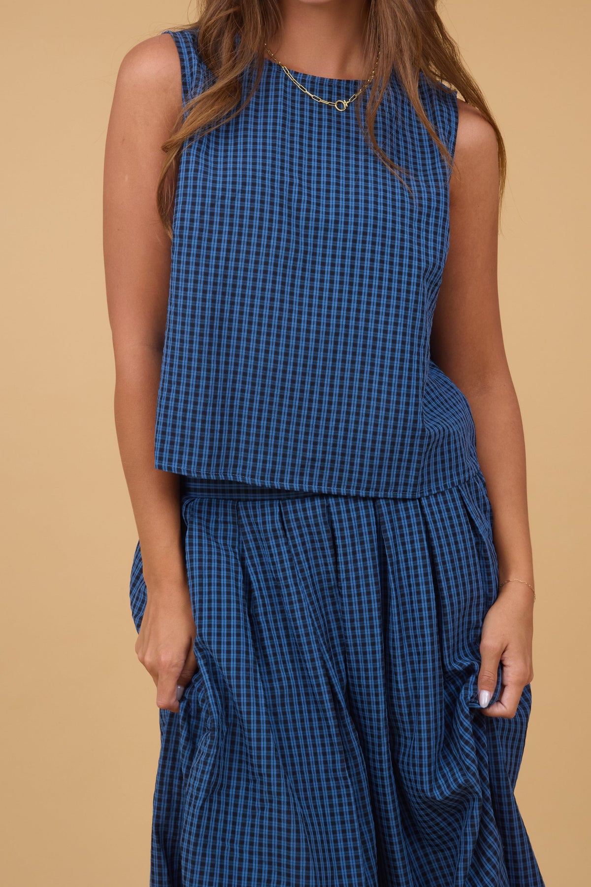 A close view of a young woman wearing a 2 piece matching set with a sleeveless swing blouse and a full pleated skirt in a navy & black plaid.