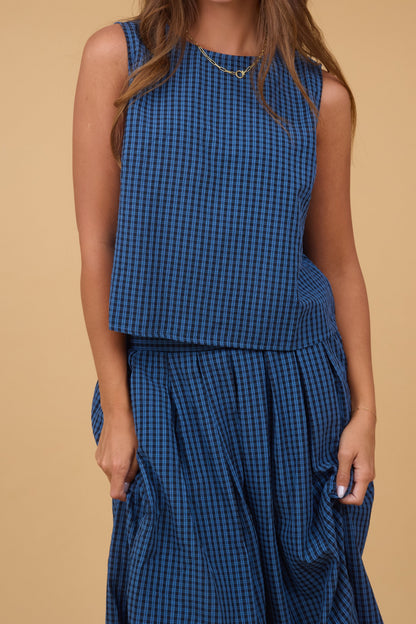 A close view of a young woman wearing a 2 piece matching set with a sleeveless swing blouse and a full pleated skirt in a navy & black plaid.