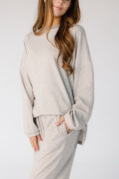 Close view of a woman wearing a loose fitting taupe lounge set with side pant pockets.