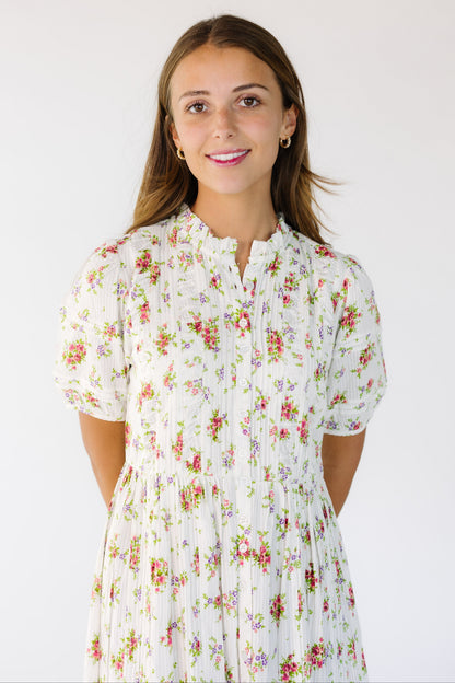 Close view of a young woman wearing a white and rose floral print dress with a high round collar with a stand up ruffle and buttons down the full length of the dress.