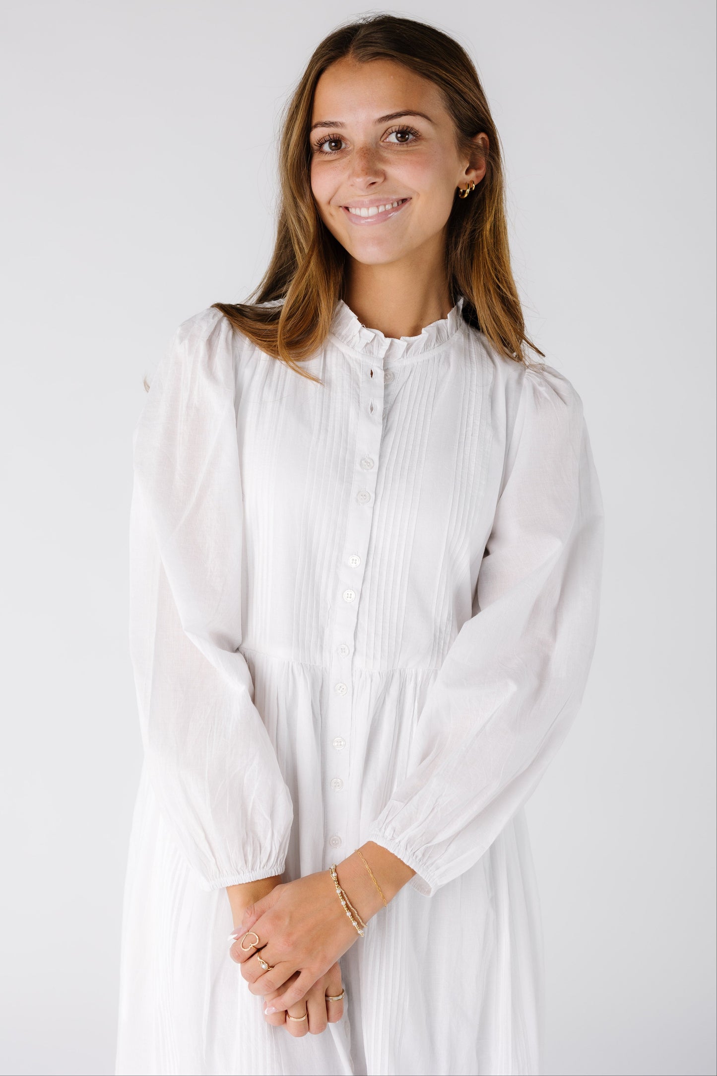 Close view of a woman wearing a white dress with a round neckline with long sleeves. 