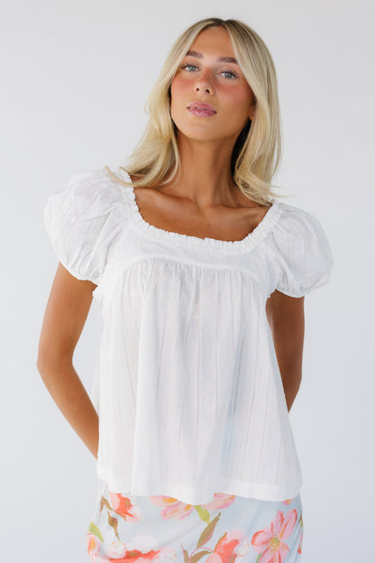 Young woman wearing a modest white Swiss dot top with a ruffled square neckline and short puff sleeves.