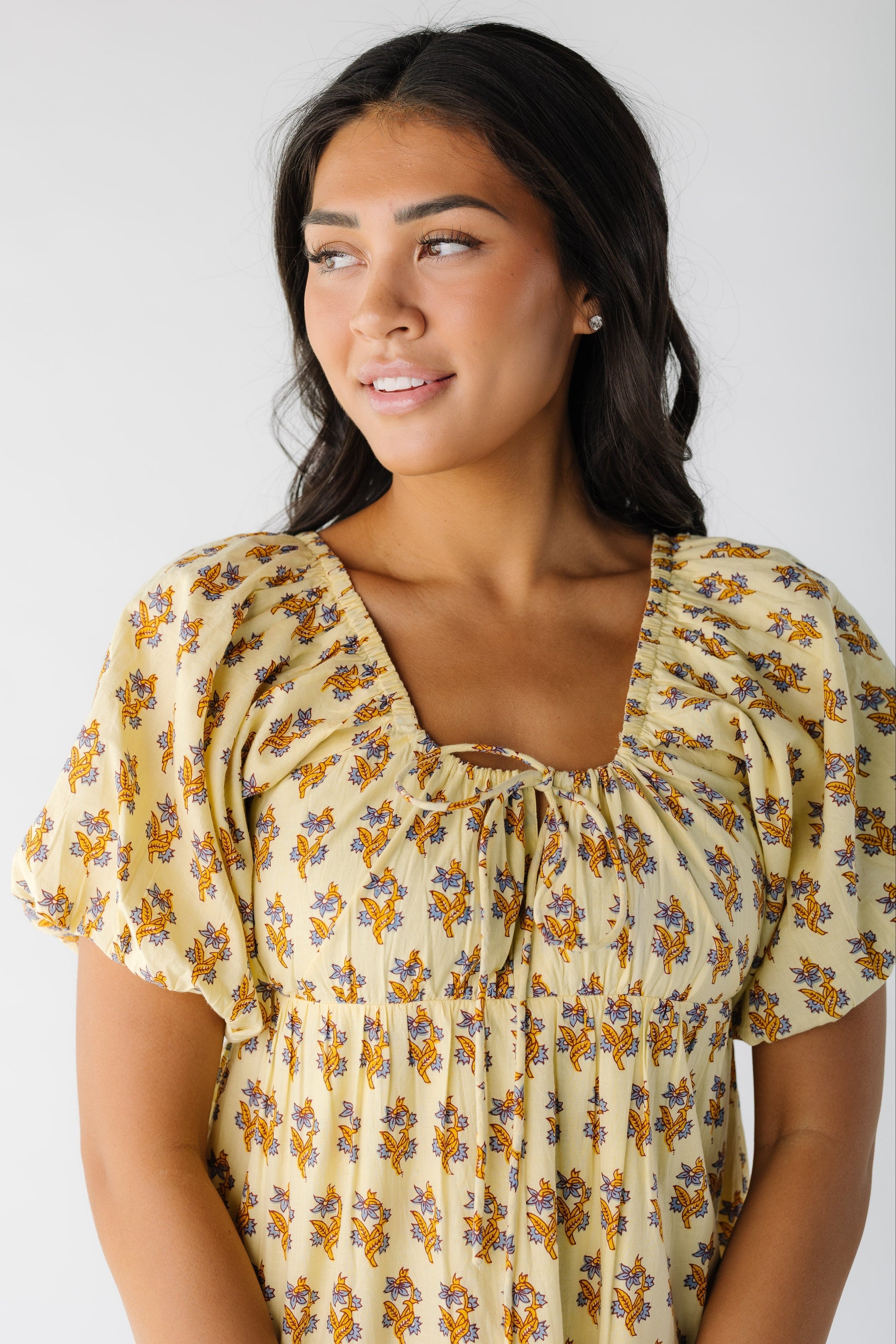 Close view of a woman wearing a yellow floral print dress with a scoop neckline and balloon sleeves.