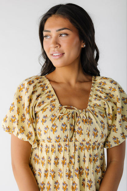 Close view of a woman wearing a yellow floral print dress with a scoop neckline and balloon sleeves.