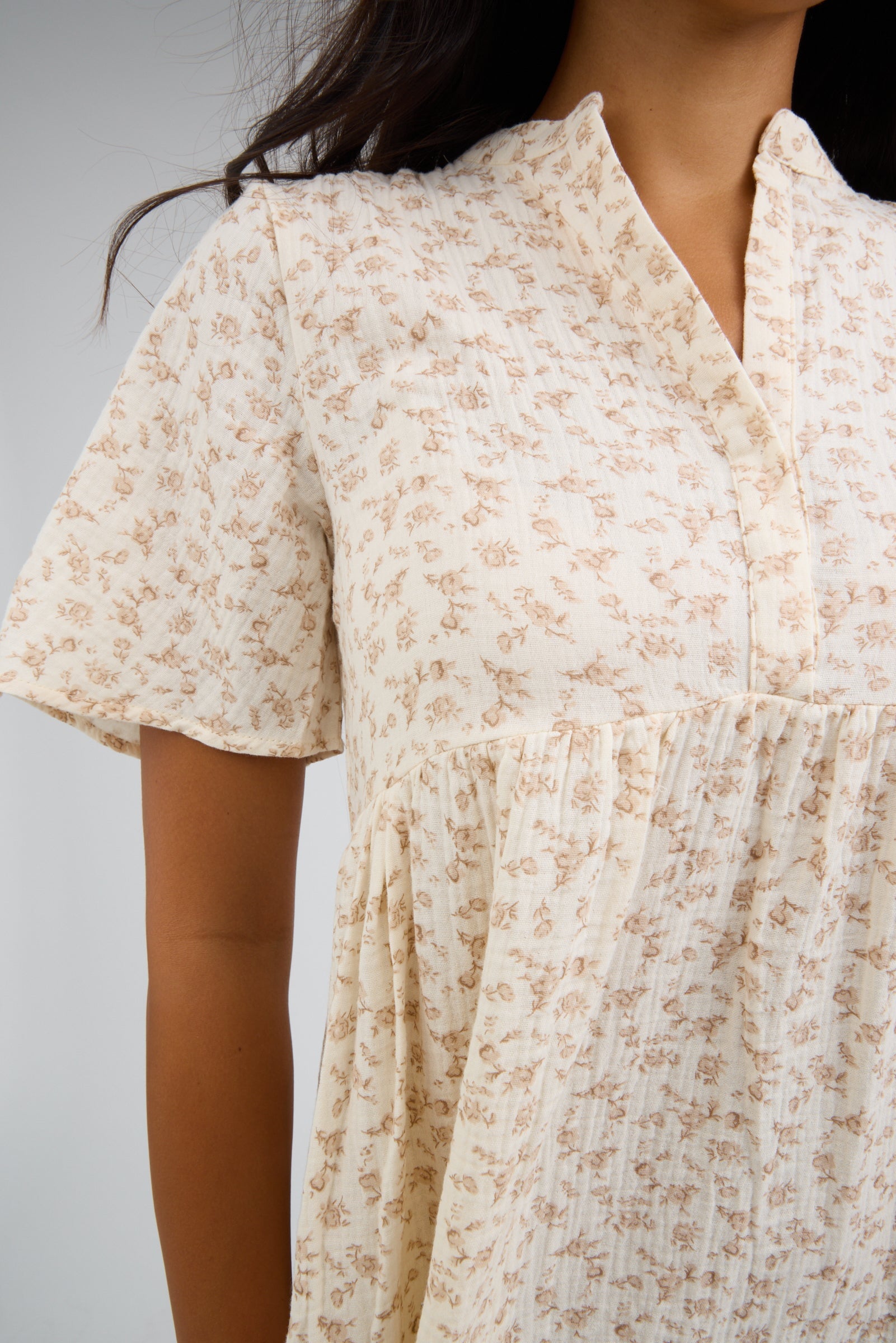 Close view of a young woman wearing an ivory floral dress with short flutter sleeves, empire waist and a V-neckline.