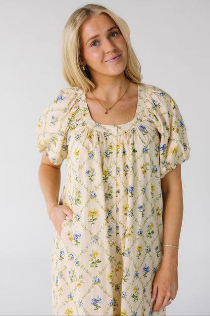 Close view of a woman wearing a loose fitting cream and multi-color floral print dress with a scoop neckline and short balloon sleeves.
