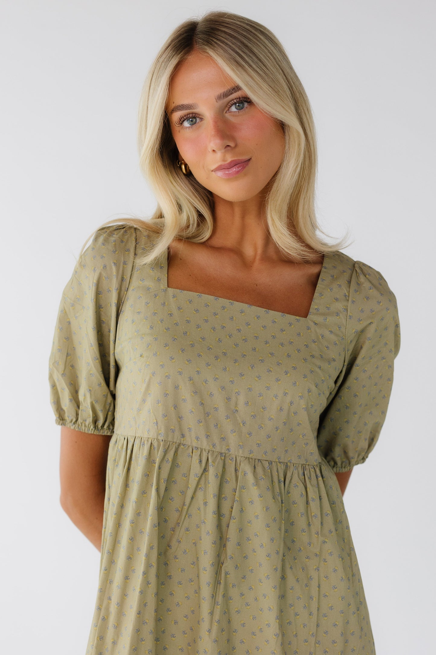 Close view of a young woman wearing a green print dress with a square neckline and puff sleeves.