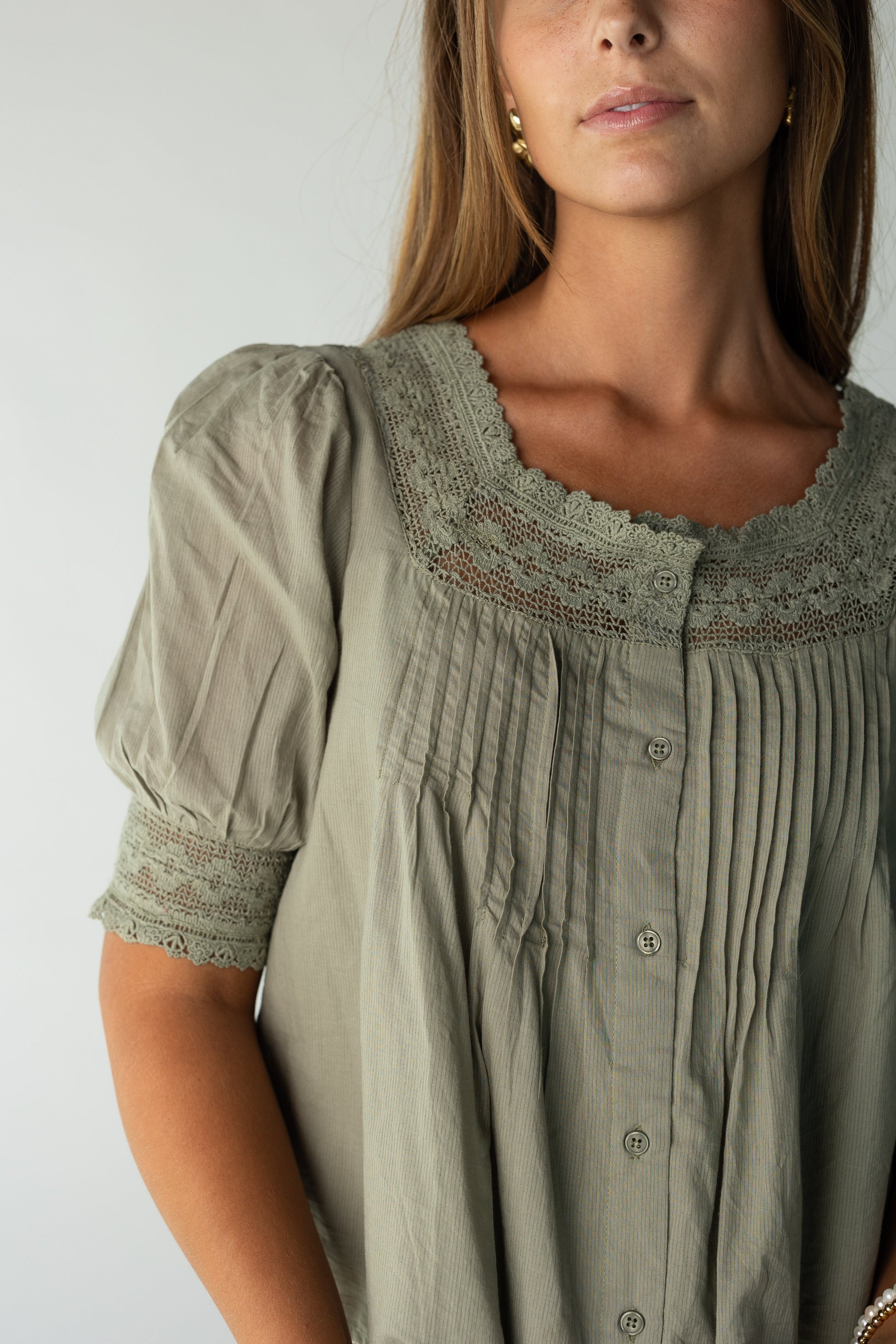 Close view of a woman wearing on olive button down top with lace neckline and cuffs