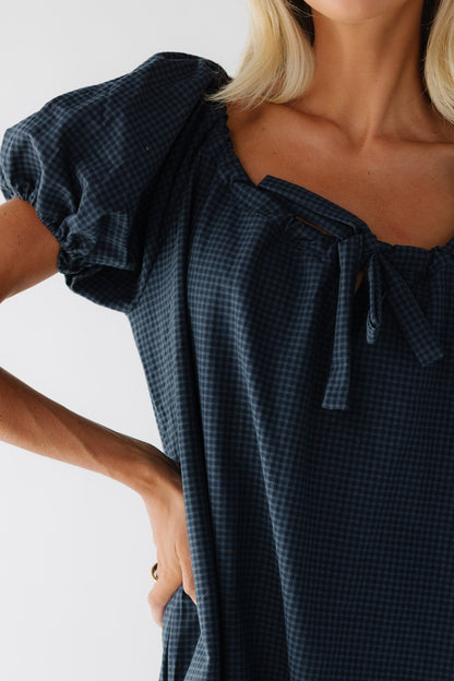 Close view of a woman wearing a navy gingham dress with short puff sleeves and drawstring neckline.