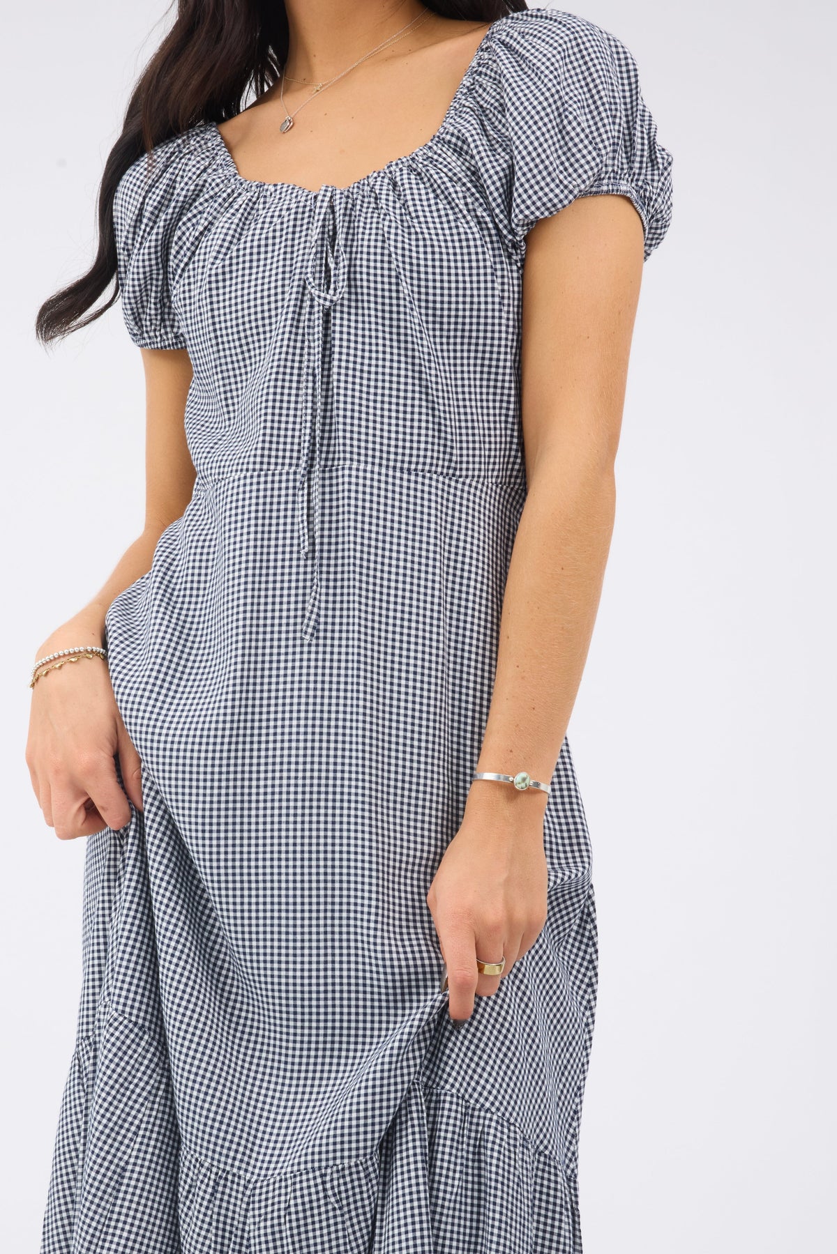 Close up view of a woman wearig a navy  white gingham midi dress with short puff sleeves and a drawstring scoop neckline.