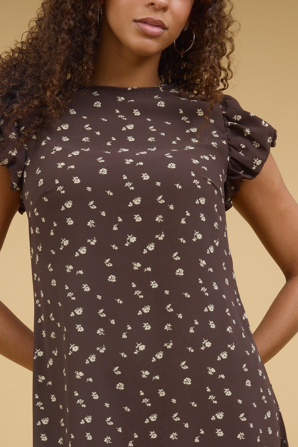Close view of a woman wearing a close fitting brown floral dress with gathered cap sleeves.