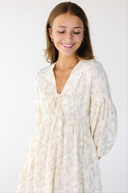 Close view of a woman wearing a cream and pink floral print dress with a V-neckline and half length sleeves.