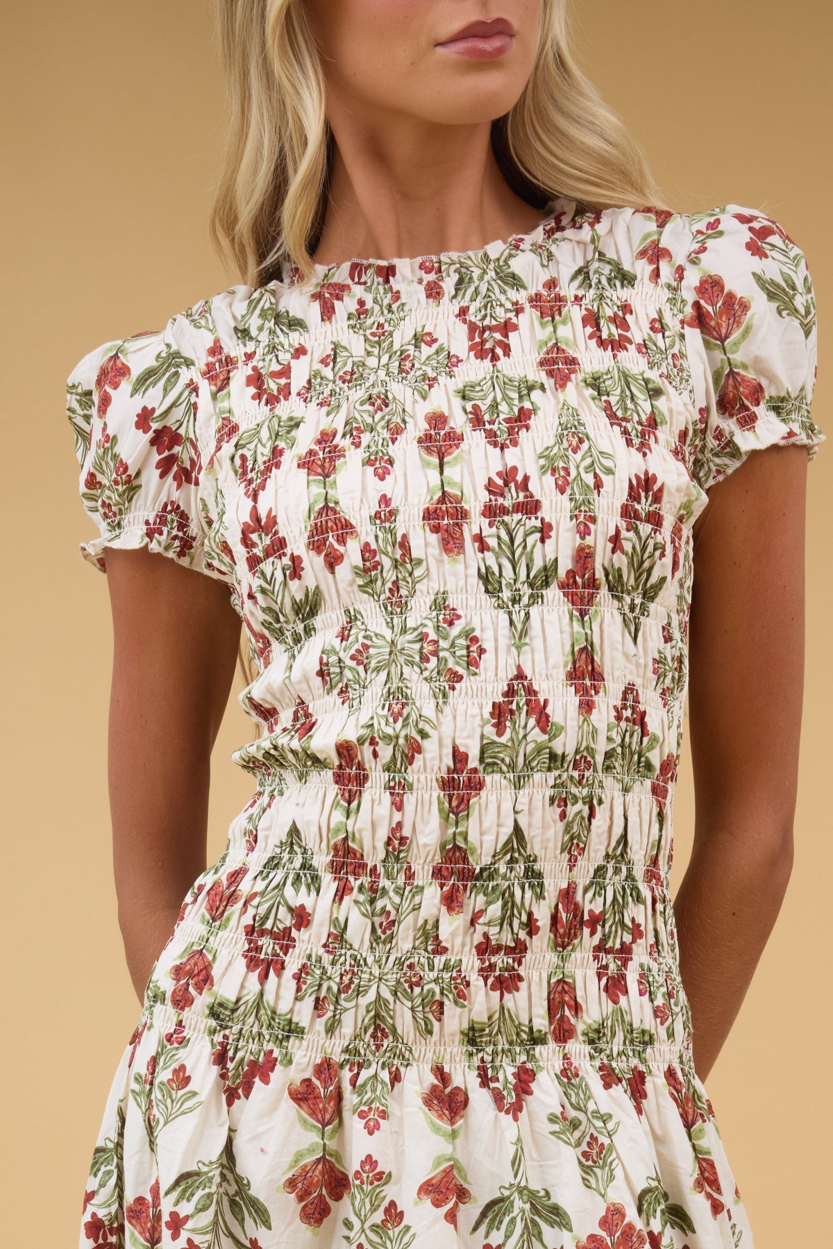 Close view of a woman wearing a cream floral dress with a long smocked bodice and short puff sleeves.