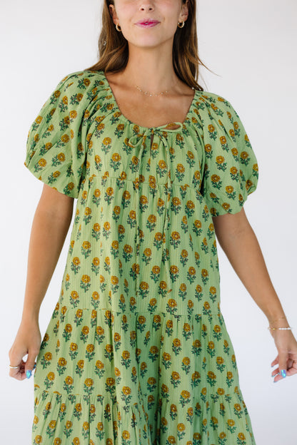 Close view of a woman wearing a loose fitting flowy  dress in a green floral print with a scoop neckline and short balloon sleeves
