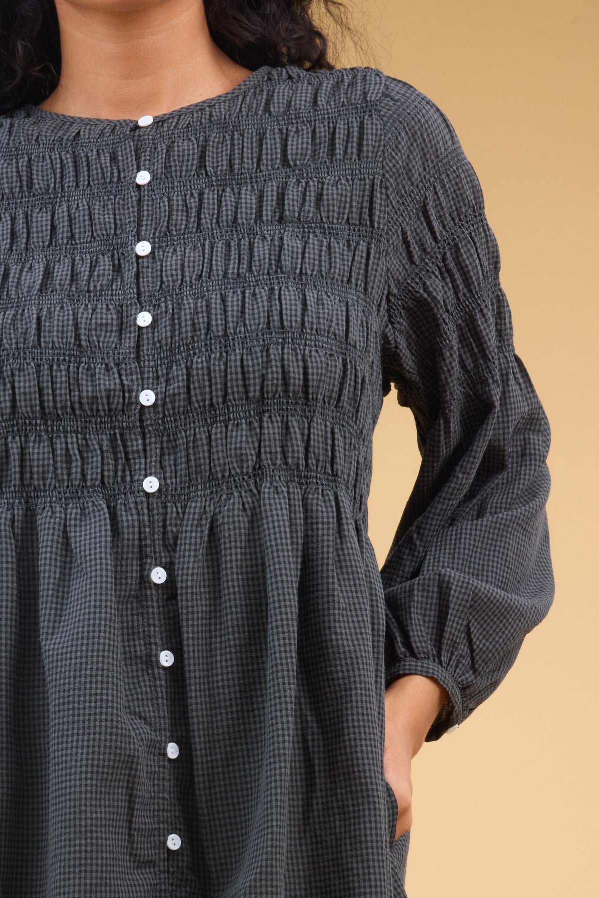 Close view of a young woman wearing a button down,  dark grey gingham dress with spaced smocking stripes, and long sleeves.