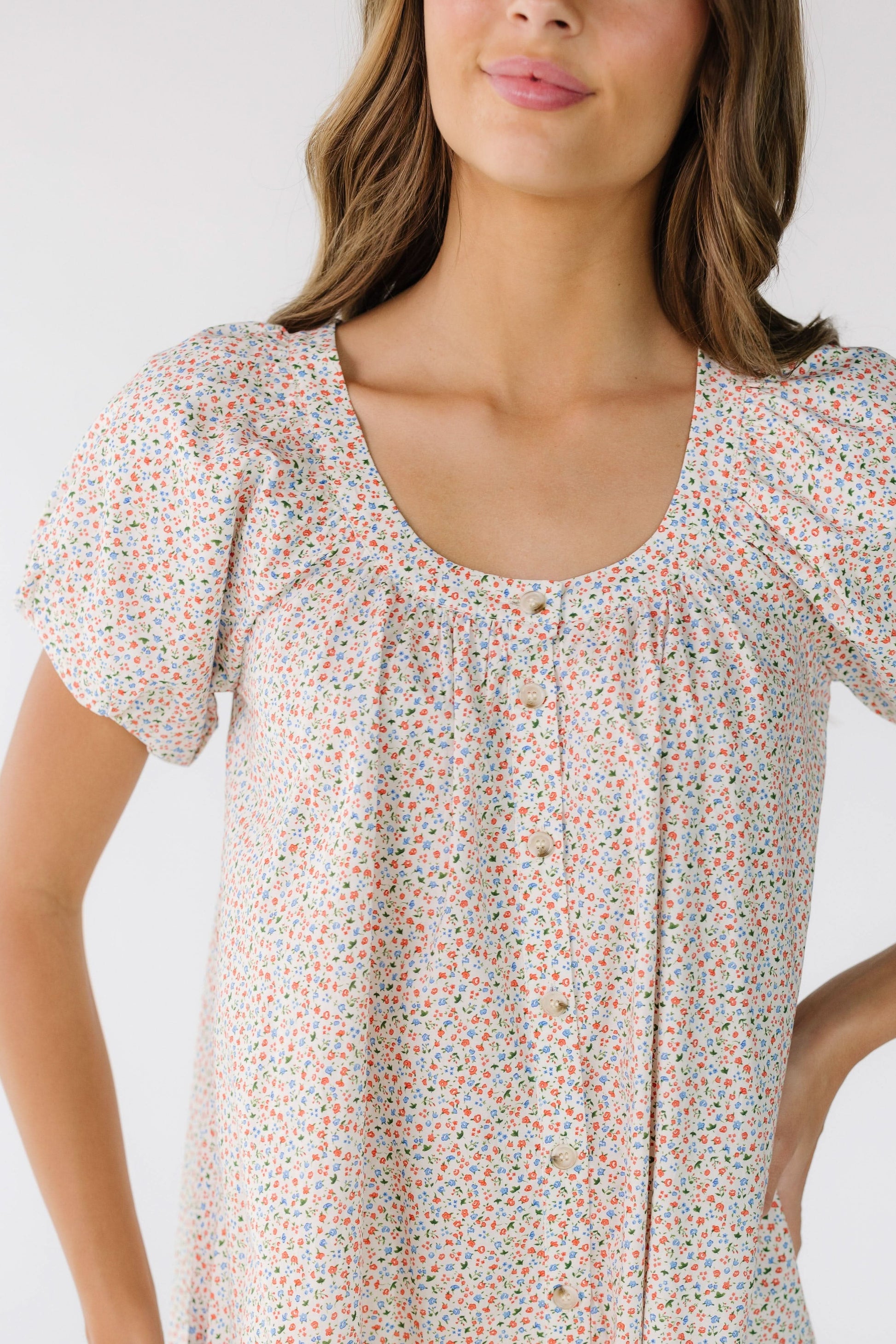 Close view of a woman wearing a white floral print dress with a scoop neckline, short puff sleeves that buttons down the front.