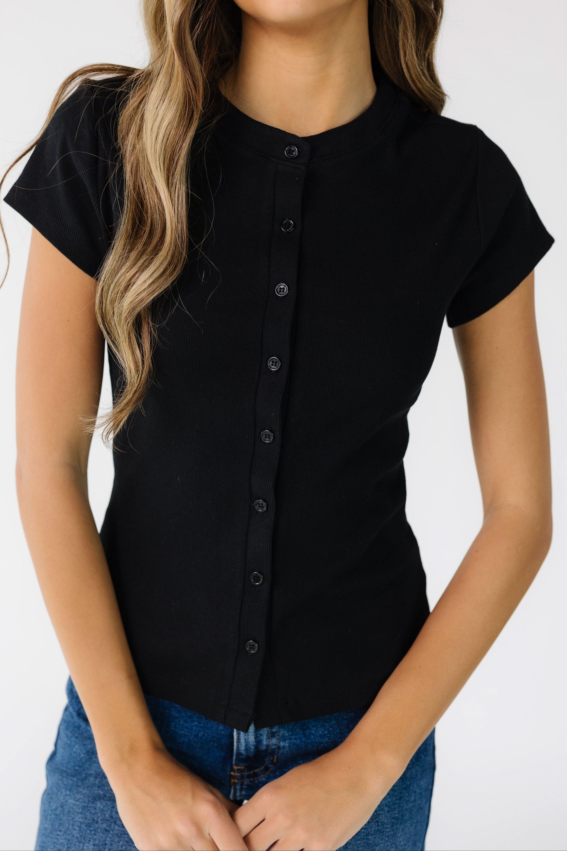 Close view of a young woman wearing a close fitting button down top with short sleeves.