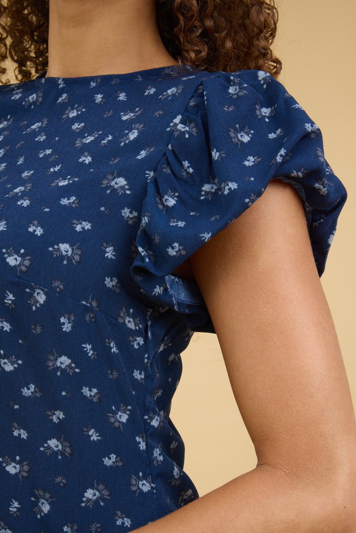 Close view of a teenage girl wearing a blue floral print dress with gathered cap sleeves.