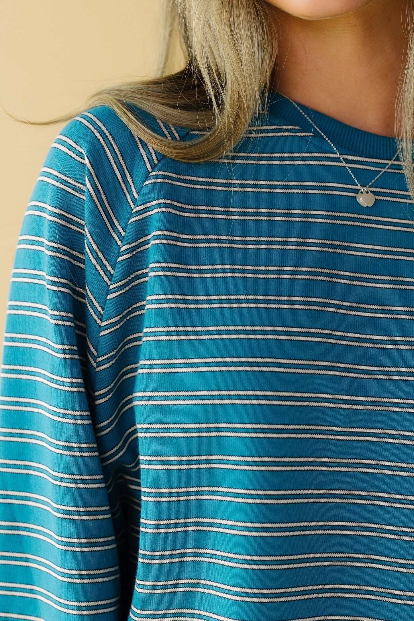 Close view of a woman wearing a teal stripe top with long sleeves.