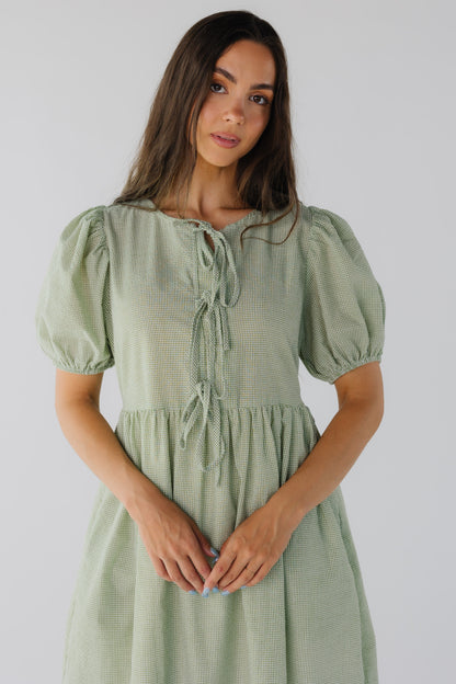 Close view of green gingham dress with round neckline, 3 tie closure and short puff sleeves