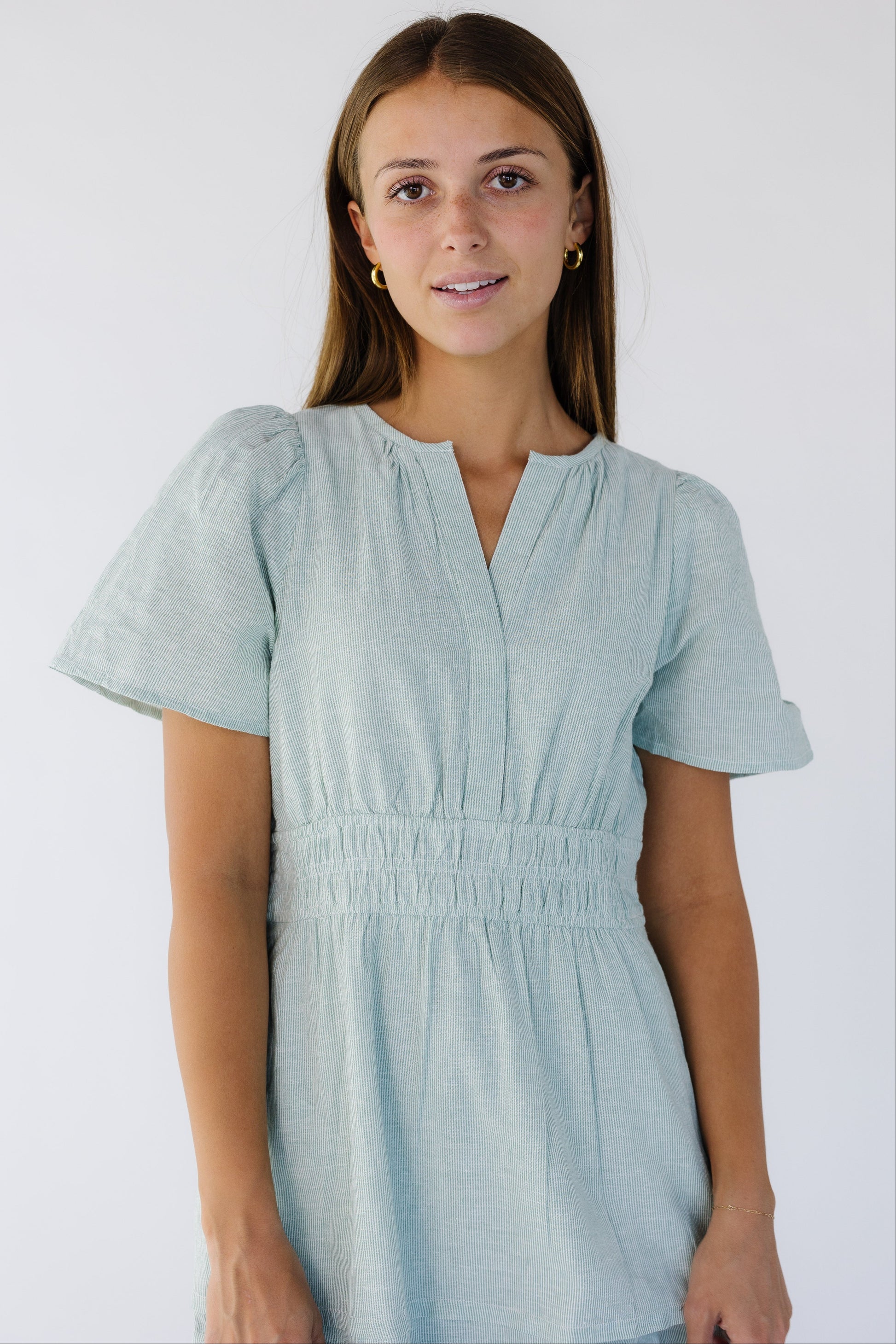 Close view of a woman wearing a green and white stripe dress with short flutter sleeves, V-neckline, and a wide 3 band elastic waist.