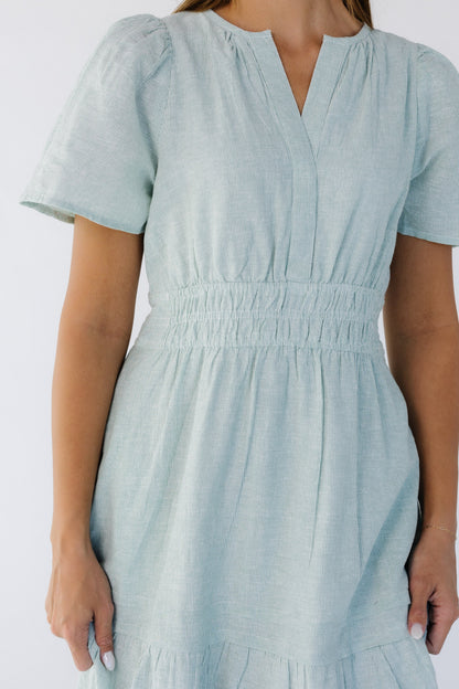 Close view of a woman wearing a green and white stripe dress with a wide 3 band elastic waist with flutter sleeves and V-neckline.