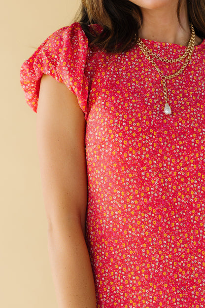 Close view of a woman wearing a red floral print dress with a round neckline and puffy cap sleeves.