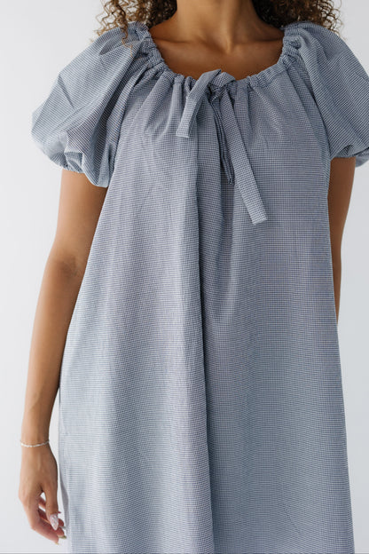 Closer view of a woman wearing a navy & white gingham short dress with balloon sleeves and a drawstring-scoop neckline.