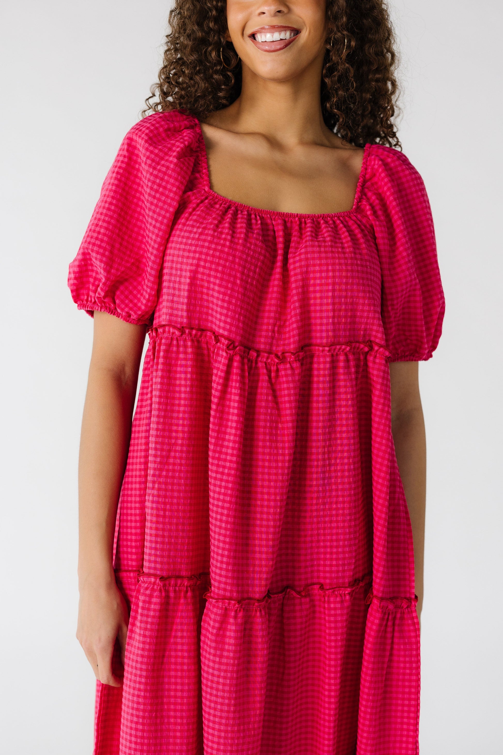 Close view of a teenage girl wearing a loose fitting pink gingham tiered dress.