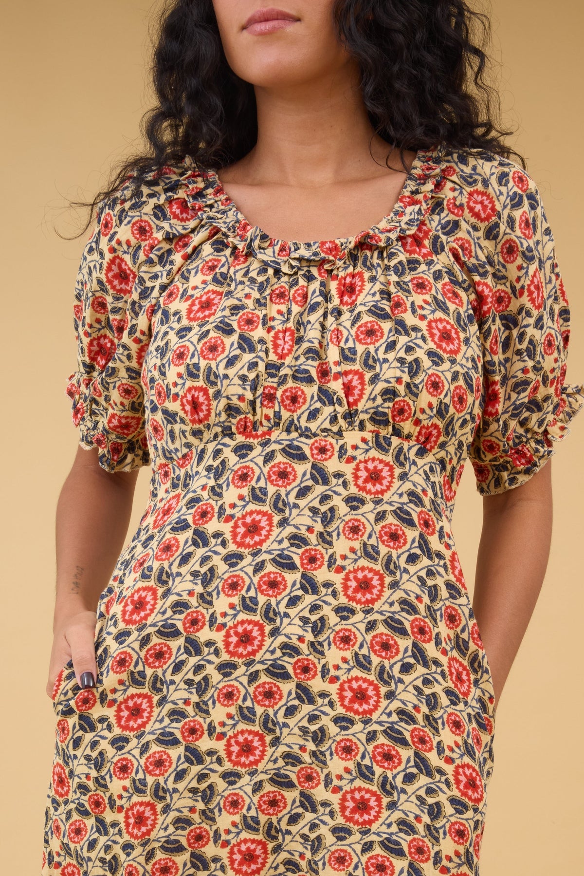 Close view of a woman wearing a floral print dress with and empire waist, gathered bodice, ruffled scoop neckline and puff sleeves.