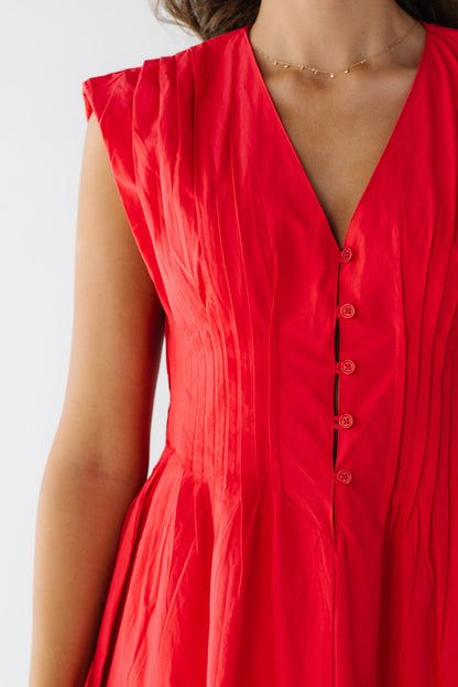 Closer view of a young woman wearing a red sleeveless dress with pleats at the shoulders and all around the waist with a short button placket with loop buttonholes.