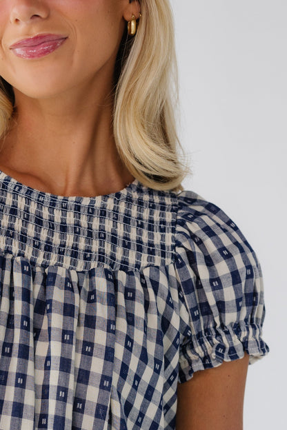 Close view of a woman wearing a navy gingham dress with puff sleeves and a smocked neckline.