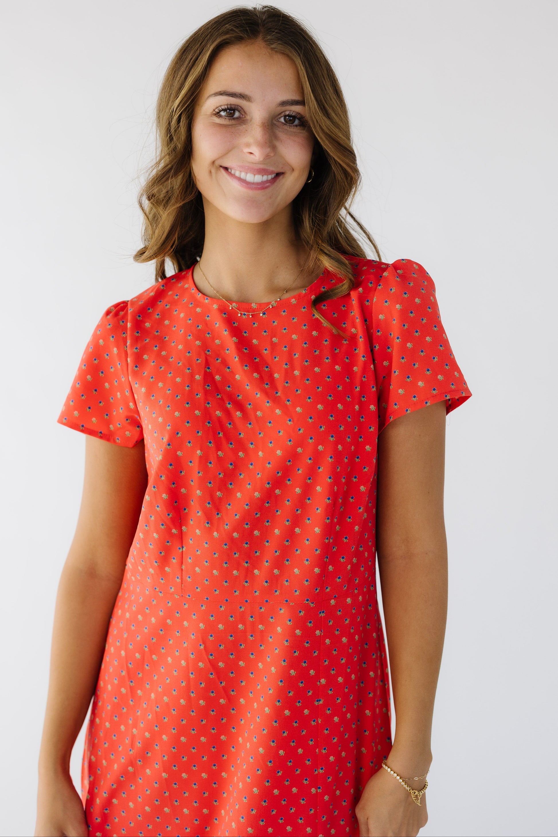 Close view of a woman wearing a red floral print sheath dress with short sleeves and a round neckline.