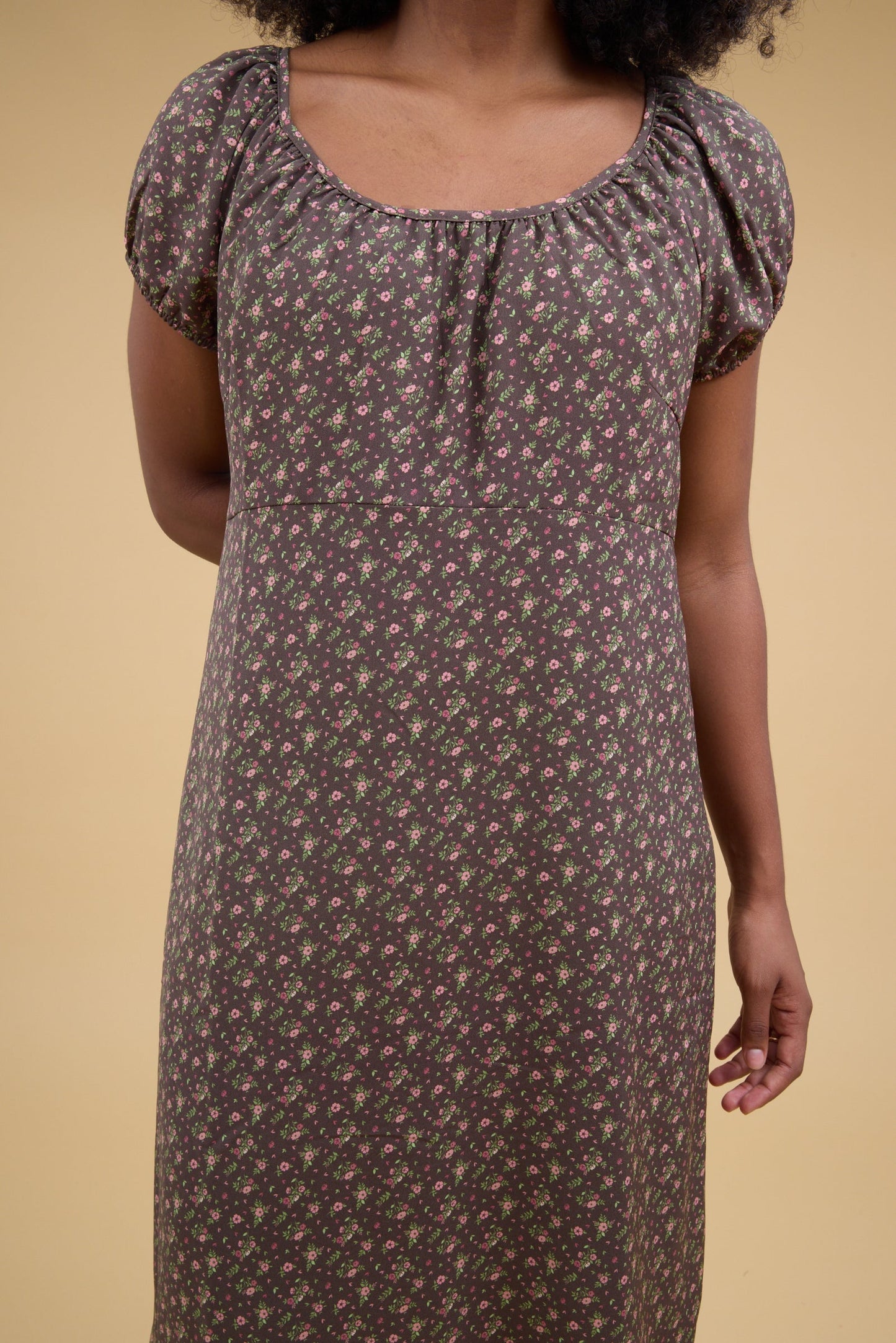 Close up view of a woman wearing an olive floral dress with short puff sleeves and wide scoop neckline.