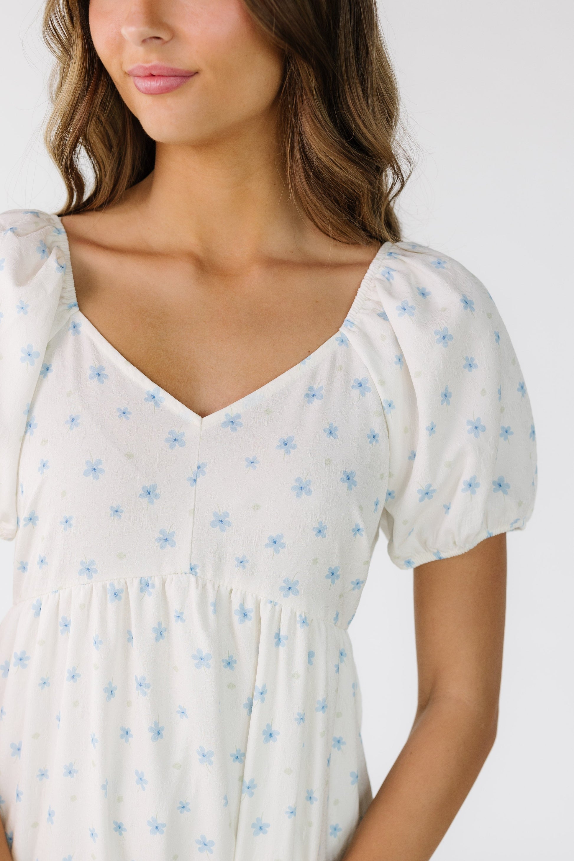 Close view of a woman wearing a white floral print dress with short puff sleeves, and a sweetheart neckline with elastic shoulders.