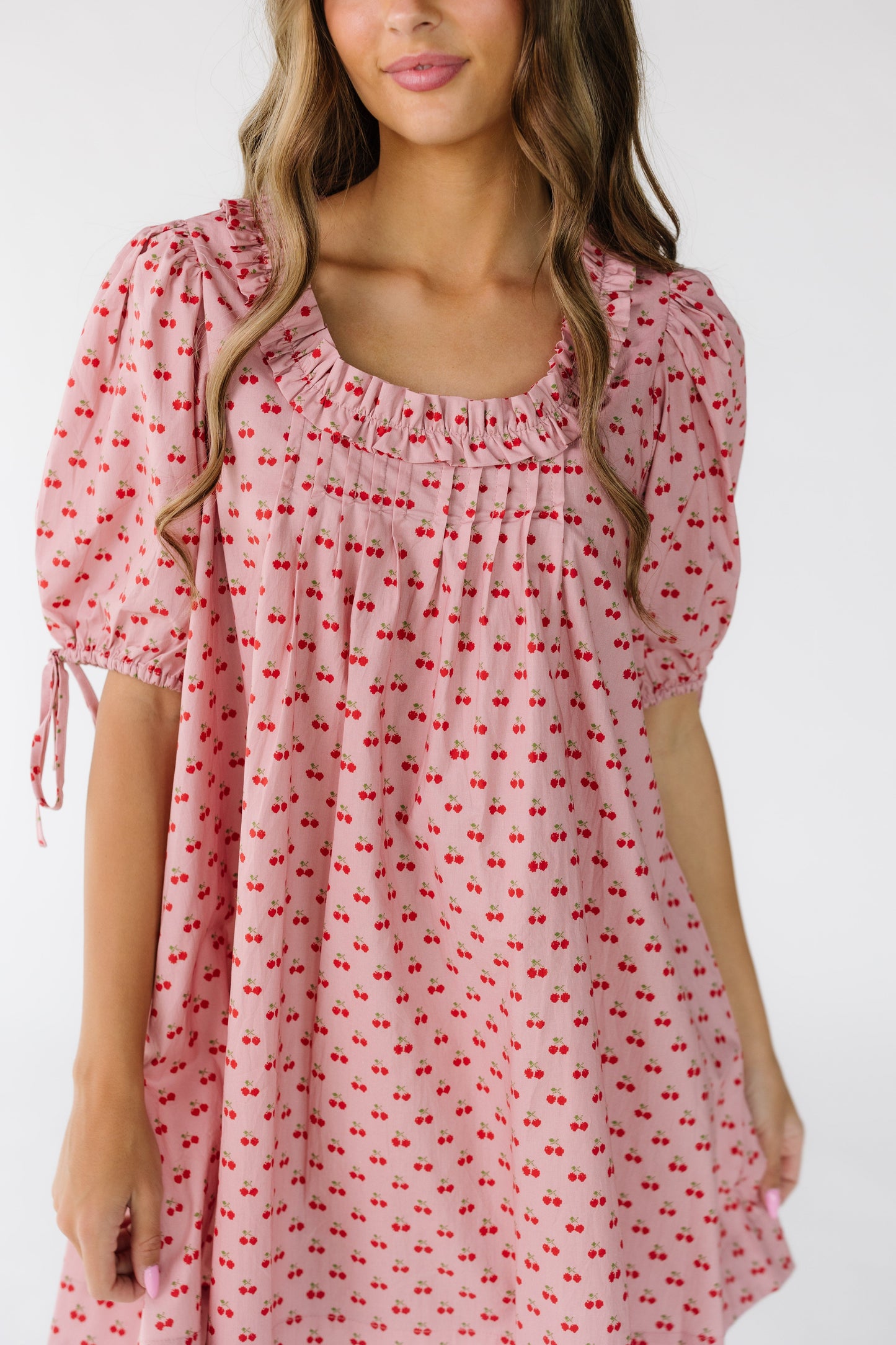 Close view of a woman wearing a short cherry print swing dress with a square neckline and front pleats.