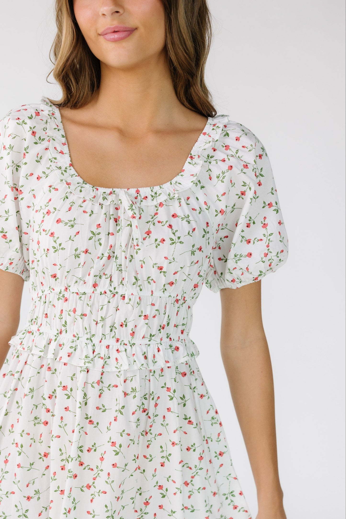 Close view of a woman wearing an ivory and red floral print with a close fitting, wide waistband and closer fitting bodice with short sleeves.
