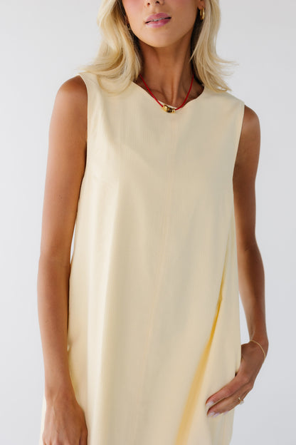 Close dress view of a woman wearing a loose fitting yellow dress with side pockets.