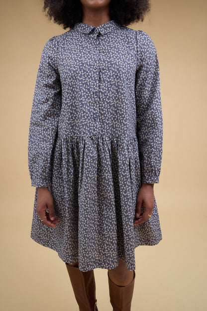 Close view of a woman wearing a charcoal  floral print dress with long sleeves, front button placket and pointed collar.