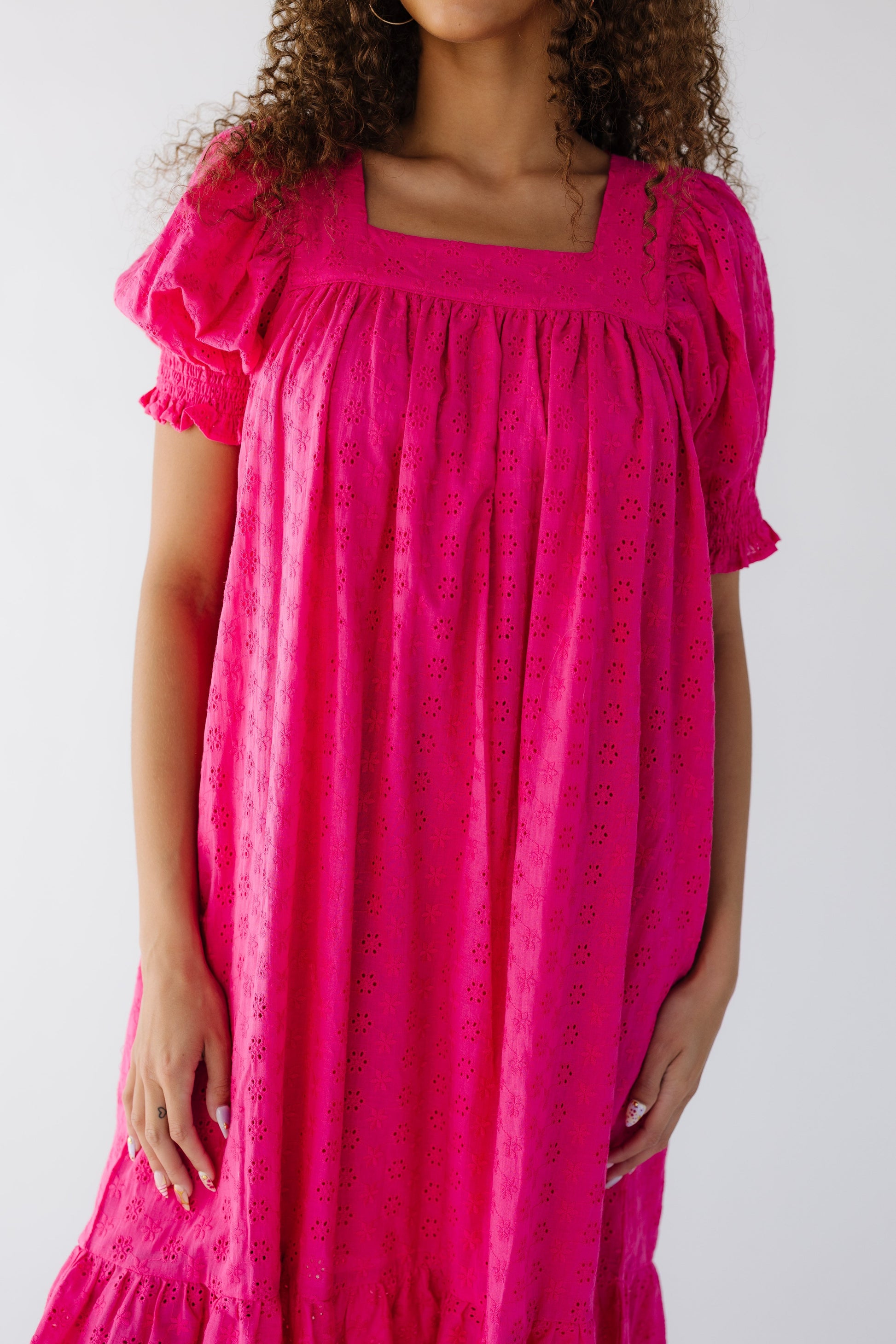 Closer view of a teen girl wearing a  deep pink eyelet midi dress with a square neckline, and puff sleeves with  smocked cuff.