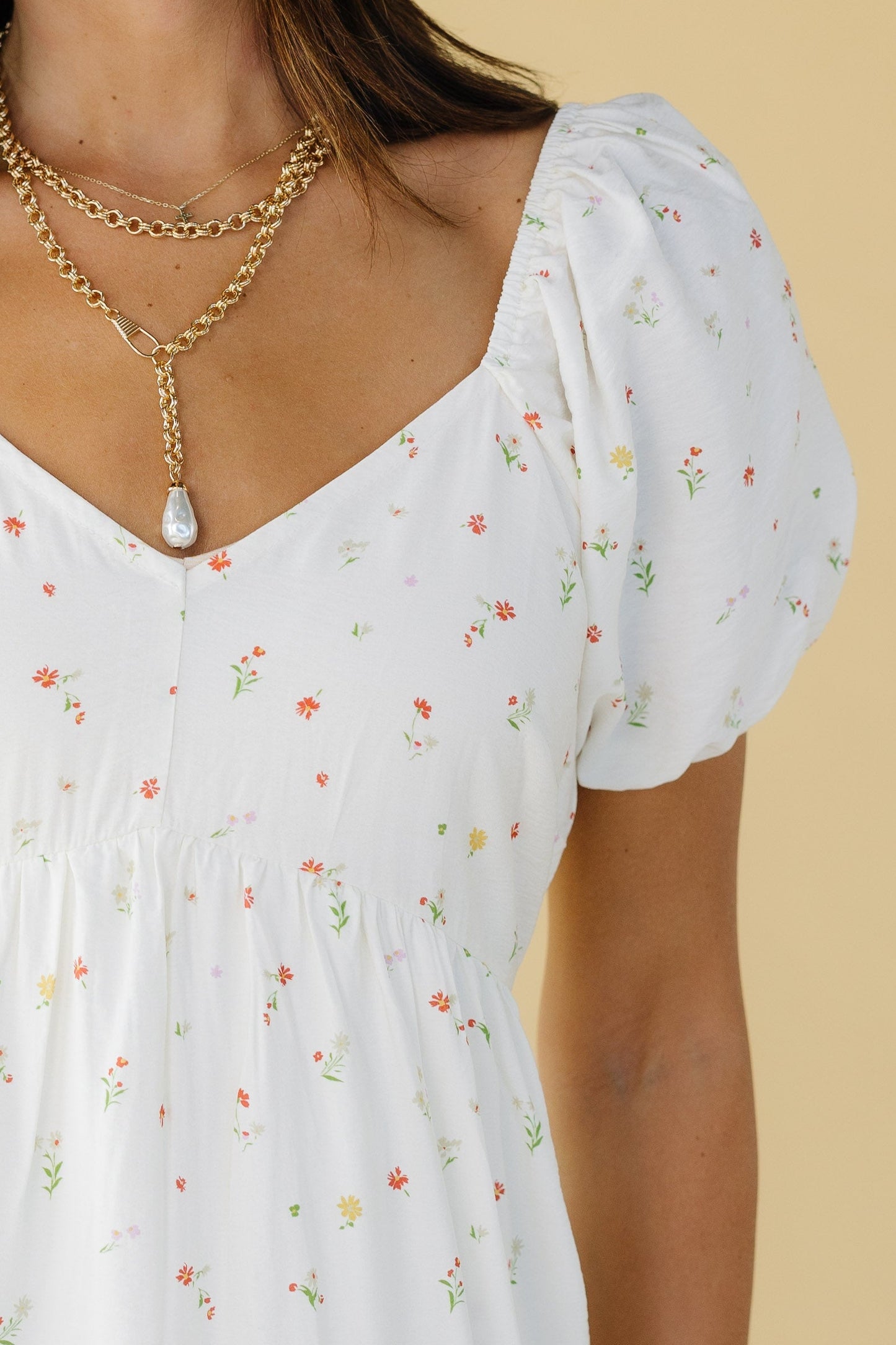 Close view of a woman wearing an off white dress with a sweetheart neckline, short puff sleeves and an empire waist.