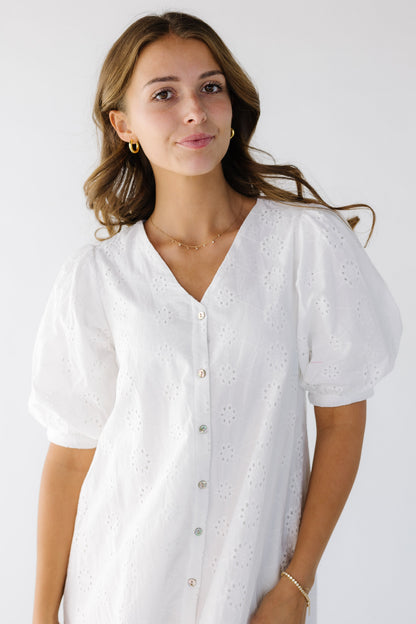 Close-up view of a young woman wearing an all white eyelet dress that buttons down the front, has a V-neckline and short balloon sleeves.