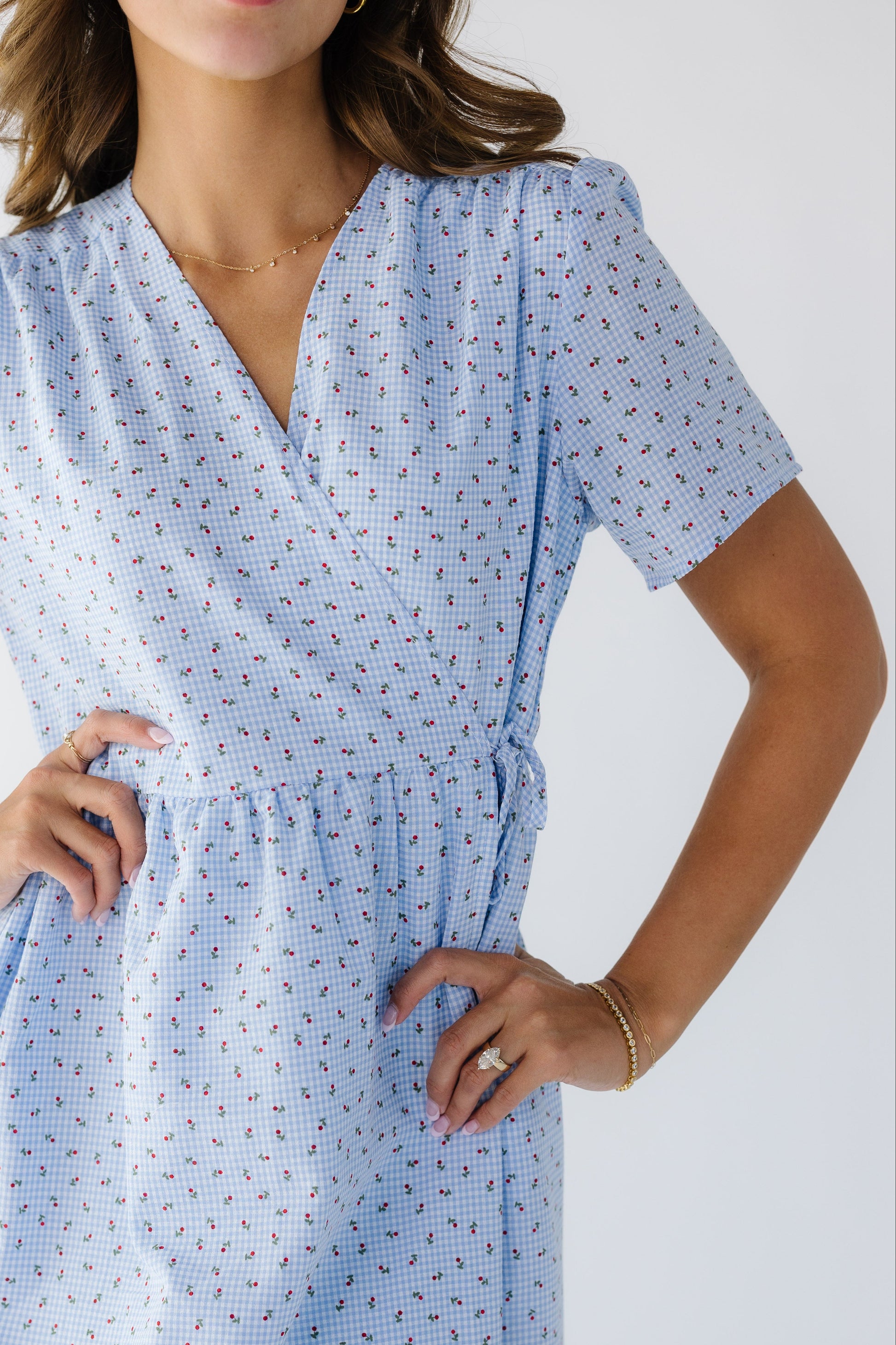 Close view of a woman wearing a floral blue gingham wrap dress with a V-neckline and short sleeves.