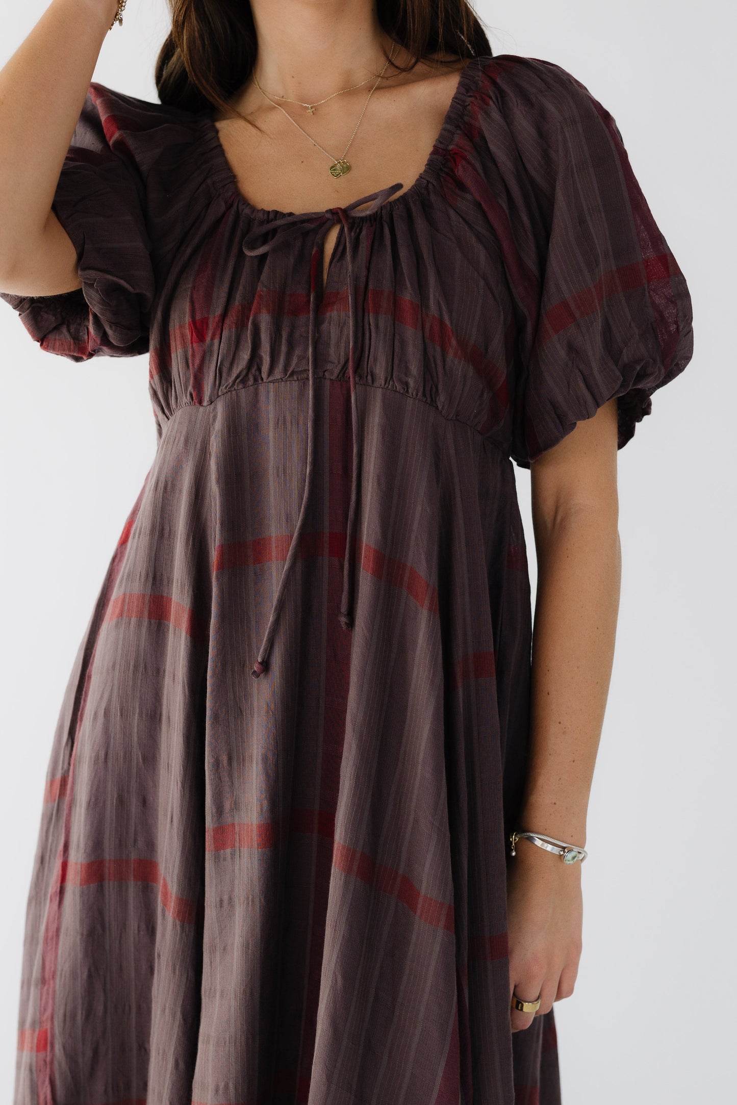 Close dress view of a young woman wearing a brown plaid dress with a full skirt, empire waist and balloon sleeves.